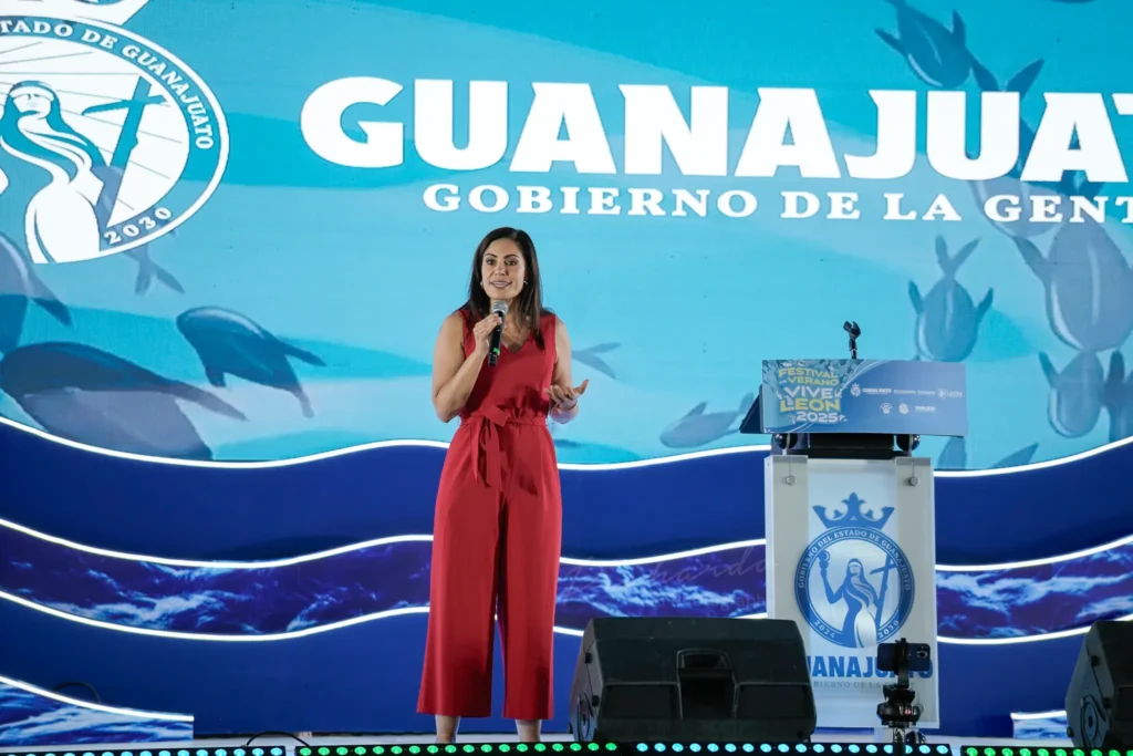 Alejandra Gutierrez, Alcaldesa de León, Guanajuato, ofreciendo discurso en pódium durante la presentación del Festival de Verano Vive León 2025 en Guanajuato. Pantalla gigante con logos de fondo