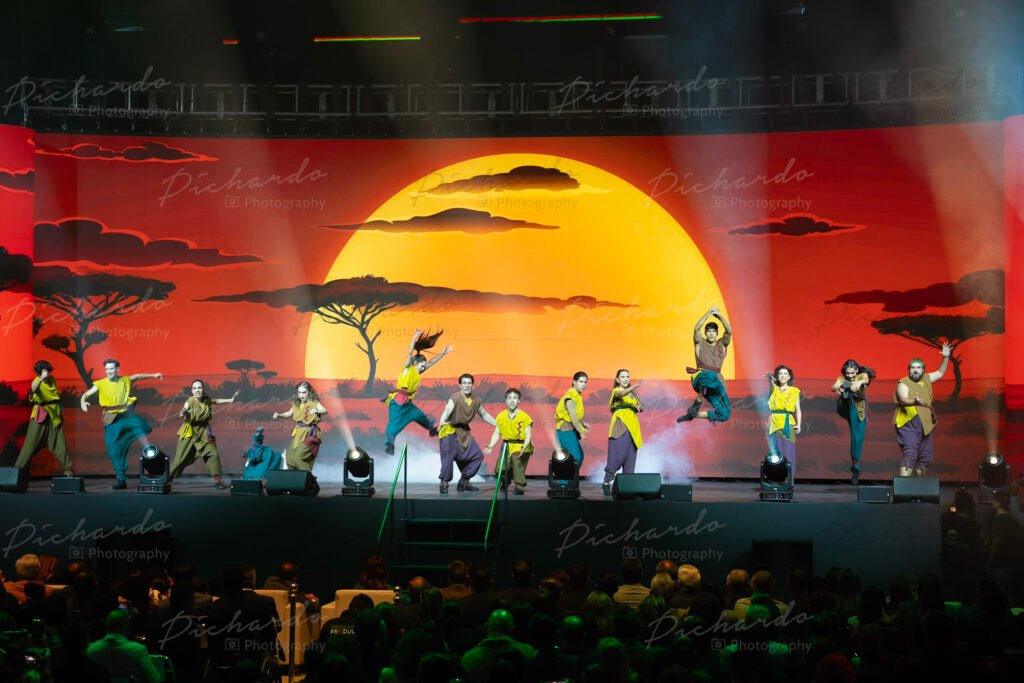 Escenario principal del espectáculo "Disney Celebra: Donde nacen los sueños" en la Feria de León 2026, mostrando el segmento de Simba y El Rey León con bailarines y atardecer en pantalla.