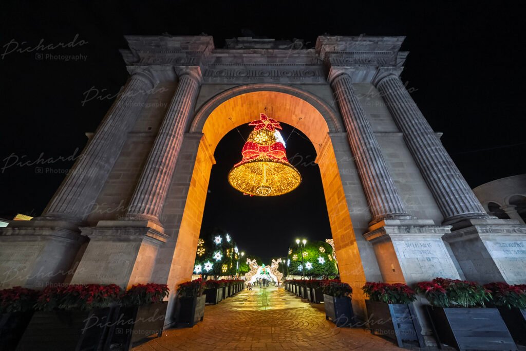 Campana monumental iluminada colgando del Arco de la Calzada en León Guanajuato con decoración de nochebuenas.