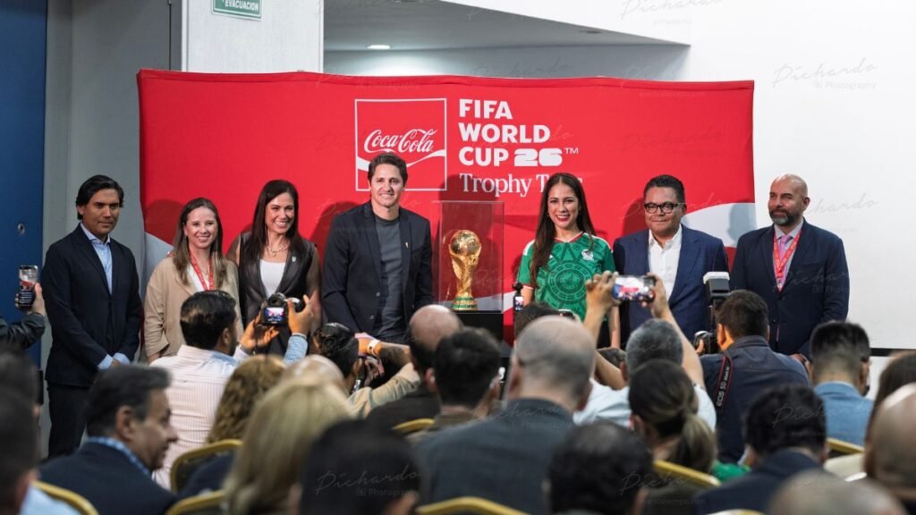 El trofeo original de la Copa Mundial de la FIFA 26 en su vitrina, acompañado por Edmílson, Libia Dennise Muñoz Ledo y Ale Gutiérrez en León.